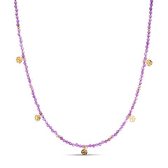 The Eva Amethyst Reversible Necklace with gold discs features handmade gold charms and vintage gemstones. Ideal for layering, this sustainable necklace illuminates in various shades of purple.